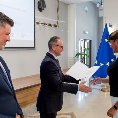 Wicemarszałek Grzegorz Boski wręcza listy gratulacyjne beneficjentom projektów energetycznych finansowanych z Unii Europejskiej. (wygenerowano przez AI)