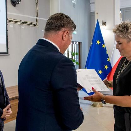 Wicemarszałek Grzegorz Boski wręcza listy gratulacyjne beneficjentom projektów energetycznych finansowanych z Unii Europejskiej. (wygenerowano przez AI)