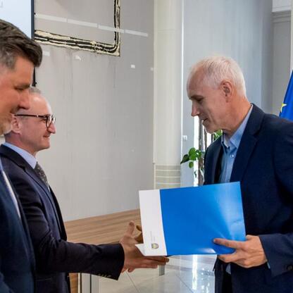 Wicemarszałek Grzegorz Boski wręcza listy gratulacyjne beneficjentom projektów energetycznych finansowanych z Unii Europejskiej. (wygenerowano przez AI)