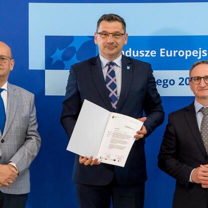 Wicemarszałek Grzegorz Boski i dwaj jego towarzysze w trakcie ceremonii wręczenia certyfikatów w ramach Europejskich Funduszy dla Śląska 2021-2027. (wygenerowano przez AI)