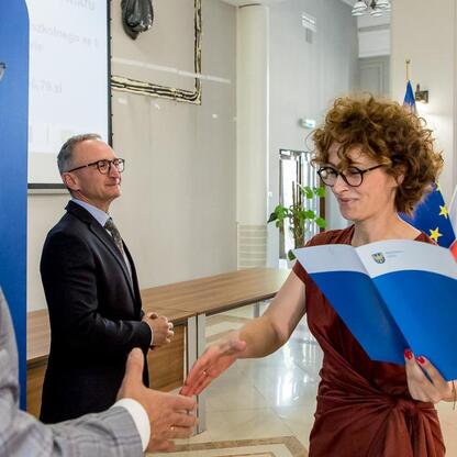 Wicemarszałek Grzegorz Boski wręcza gratulacje beneficjentom projektów energetycznych finansowanych z Unii Europejskiej. (wygenerowano przez AI)
