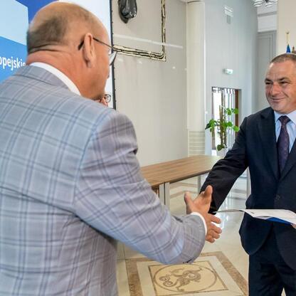 Dwa mężczyźni w strojach formalnych trzymają się za ręce w profesjonalnym środowisku, związany z funduszami europejskimi dla Śląska. (wygenerowano przez AI)