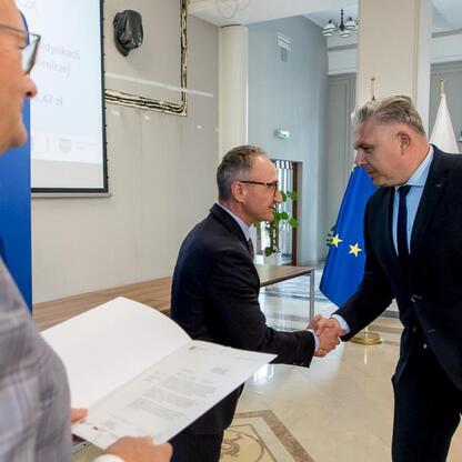 Wicemarszałek Grzegorz Boski wręcza listy gratulacyjne beneficjentom projektów energetycznych finansowanych z Unii Europejskiej. (wygenerowano przez AI)