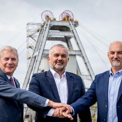 Grupa czterech mężczyzn w formalnym stroju stoi przed przemysłowym budynkiem, uczestnicząc w briefingu prasowym. (wygenerowano przez AI)