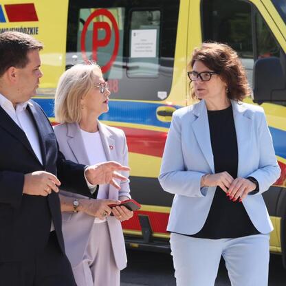 Zdjęcie przedstawia trzech ludzi w biznesowych strojach przed samochodem ratowniczym Wojewódzkiego Pogotowia Ratunkowego w Zabrzu. (wygenerowano przez AI)