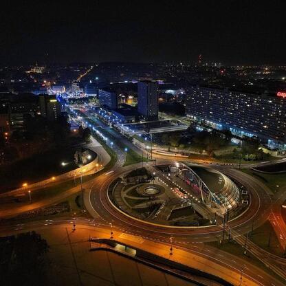 Zdjęcie przedstawia nocny widok Ronda Sztuki w Katowicach, oświetlonego i otoczonego nowoczesnymi budynkami. (wygenerowano przez AI)