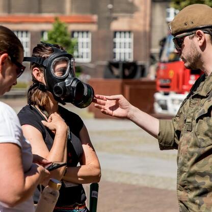 Grupa uczestników wzięła udział w szkoleniu organizowanym przez Śląskie Oddział Straży Granicznej i 13 Śląskiej Brygady Obrony Terytorialnej. Osoby w gazowych maskach uczestniczą w symulacji, podczas  (wygenerowano przez AI)