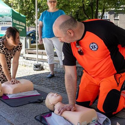 Praktyczne ćwiczenia CPR na manekinach, z zewnątrz, w otoczeniu budynku Urzędu Marszałkowskiego Województwa Śląskiego. (wygenerowano przez AI)