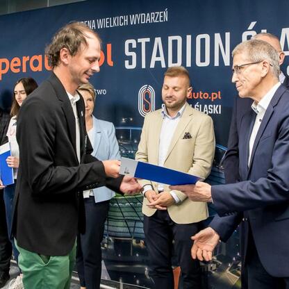 Na zdjęciu przedstawiono ceremonię w Superauto.pl Stadion Śląski, gdzie osoby w strojach formalnych uczestniczą w uroczystości związanych z kulturą fizyczną i bezpieczeństwem publicznym. (wygenerowano przez AI)