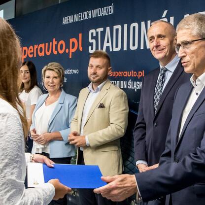 Wicemarszałek Leszek Pietraszek prezentuje certyfikaty na ceremonii w Superauto.pl Stadion Śląski. (wygenerowano przez AI)