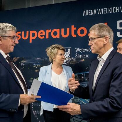 Formalna ceremonia w Superauto.pl Stadion Śląski, gdzie osoby w strojach formalnych przekazują dokumenty i składają gratulacje. (wygenerowano przez AI)