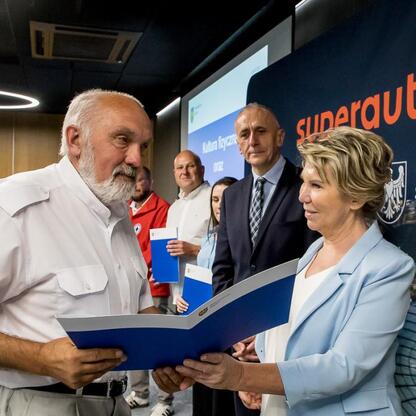 Wicemarszałek Leszek Pietraszek prezentuje dokumenty, symbolizujące transfer umów, w Superauto.pl Stadion Śląski. (wygenerowano przez AI)
