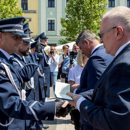 Na rynku w Rybniku w trakcie uroczystości Święta Policji w Śląskim Voivodztwie, policjant wręcza dokument, symbolizując nagrodę lub uznanie. (wygenerowano przez AI)