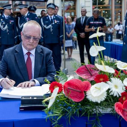 Formalna uroczystość na rybnickim rynku z okazji Święta Policji w 2023 roku. Funkcjonariusze i samorządowcy uczestniczą w ceremonii, podpisując dokumenty i wręczając odznaczenia. (wygenerowano przez AI)