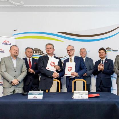 Grupa mężczyzn w strojach formalnych podpisuje dokumenty, uczestnicząc w ważnym projekcie infrastrukturalnym w Sławkowie, Polska. (wygenerowano przez AI)