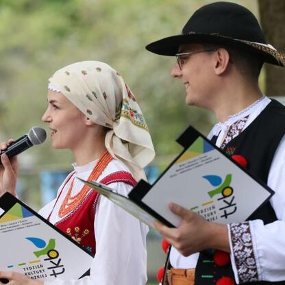 Dwa uczestnicy Tydzień Kultury Beskidzkiej w tradycyjnych strojach, z mikrofonem i notatkami. (wygenerowano przez AI)