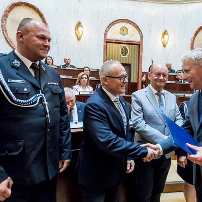 Wojciech Saługa, Marszałek Województwa Śląskiego, wręcza dokument uniformowanemu oficerowi, symbolizującemu transfer promes na dostawę nowych wozów strażackich. (wygenerowano przez AI)