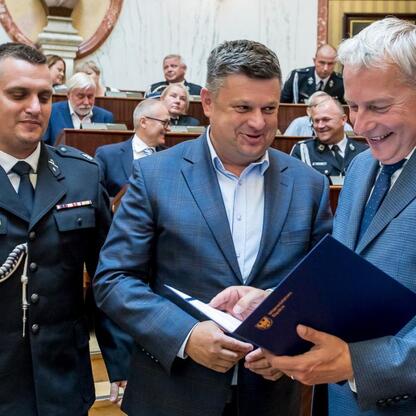 Wojciech Saługa, Marszałek Województwa Śląskiego, prezentuje dokumenty na ceremonii przekazania 33 nowych wozów ratowniczo-gaśniczych dla OSP w regionie. (wygenerowano przez AI)