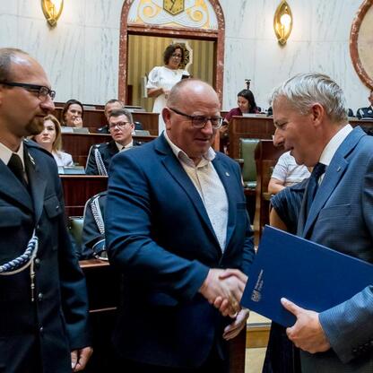 Wojciech Saługa, Marszałek Województwa Śląskiego, wręcza dokumenty na ceremonii dostawy nowych wozów strażackich. (wygenerowano przez AI)