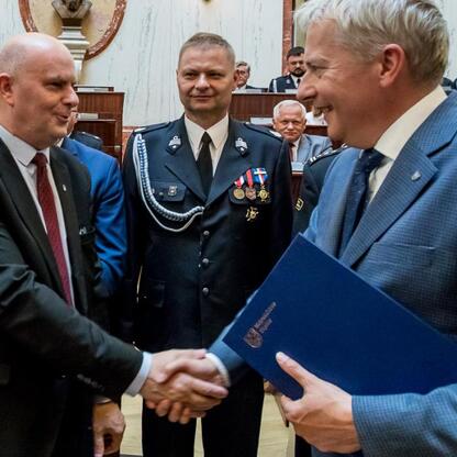 Wojciech Saługa i Rafał Adamczyk podczas ceremonii wręczenia nowych wozów strażackich. (wygenerowano przez AI)