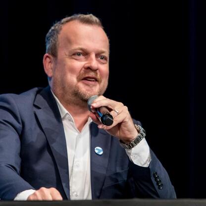 Mężczyzna w garniturze, przemawiający na konferencji o modernizacji Teatru Zagłębia w Sosnowcu. (wygenerowano przez AI)