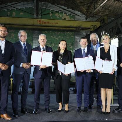 Grupa dziewięciu osób, w tym Wojciech Saługa, marszałek Województwa Śląskiego, stoi razem w przemysłowej lokalizacji, podczas ceremonii związanych z budową nowego centrum gamingowo-technologicznego. (wygenerowano przez AI)