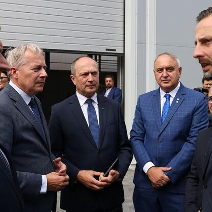 Grupa men w garniturach przed modernistycznym budynkiem Bumar-Łabędy w Gliwicach, podpisują umowę o produkcję K2. (wygenerowano przez AI)