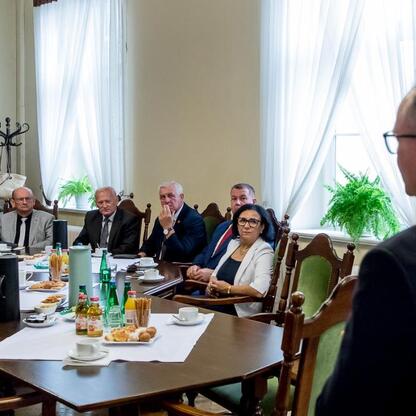 Formalne spotkanie w pomieszczeniu z dużymi oknami, gdzie ludzie w strojach biznesowych omawiają projekty scalania gruntów. (wygenerowano przez AI)