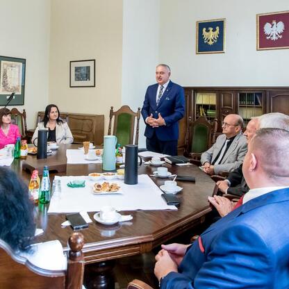 Formalna sesja w konferencyjnym pomieszczeniu, gdzie rozmawia się o programie scalania gruntów w powiatach raciborskim, częstochowskim i zawierciańskim. (wygenerowano przez AI)