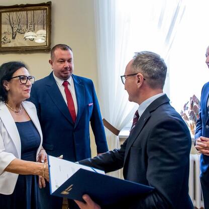Formalna ceremonia województwa śląskiego, gdzie osoby w strojach formalnych wymieniają dokumenty, związana z programem scalania gruntów rolnych. (wygenerowano przez AI)
