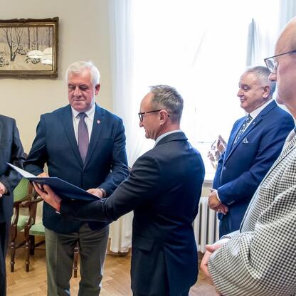 Wicemarszałek Grzegorz Boski wręcza listy gratulacyjne radnym Sejmiku za dofinansowanie projektów scalania gruntów w powiatach raciborskim, częstochowskim i zawierciańskim. (wygenerowano przez AI)