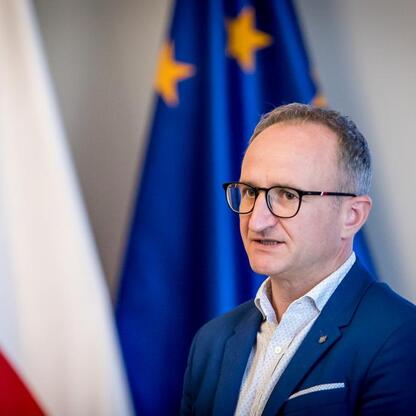 Wicemarszałek Grzegorz Boski przed flagami UE w Sali Błękitnej Gmachu Sejmu Śląskiego. (wygenerowano przez AI)