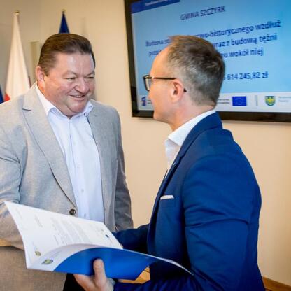Dwa mężczyźni w strojach formalnych przekazują dokument, prawdopodobnie w kontekście finansowania projektów turystycznych i kulturalnych w regionie Śląskim. (wygenerowano przez AI)