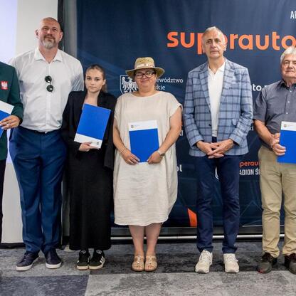 Grupa sześciu osób w formalnej odzieży, trzymających niebieskie foldery, przedstawiająca nagrody sportowe dla najlepszych sportowców w 2024 roku, organizowane przez Województwo Śląskie. (wygenerowano przez AI)