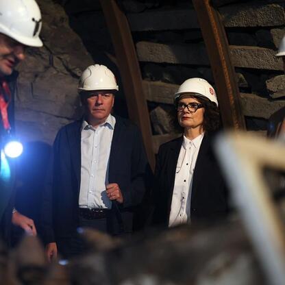 Grupa osób w profesjonalnym stroju i hard hatach inspektuje historyczny zabytek górniczy, promując jego turystyczne znaczenie. (wygenerowano przez AI)