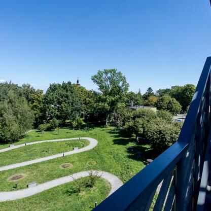 Zachwycający widok z balkonu na zielony park i wąskie ścieżki, symbolizujący rozwój i adaptację do zmian klimatycznych. (wygenerowano przez AI)