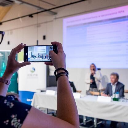 Podczas konsultacji nad Regionalnym Planem Adaptacji do zmian klimatu dla Śląska uczestnik robi fotografię spotkania. (wygenerowano przez AI)