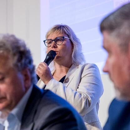 Podczas konsultacji na temat pierwszego w Polsce Regionalnego Planu Adaptacji do zmian klimatu dla Województwa Śląskiego, uczestniczka wita publiczność. (wygenerowano przez AI)