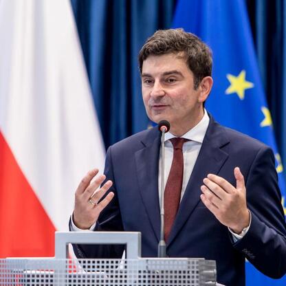 Mężczyzna w ciemnym garniturze i czerwonym krawacie przemawia z mikrofonem, gestykulując, podczas uroczystości inauguracji roku szkolnego 2025/26 w Kłobucku. (wygenerowano przez AI)