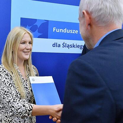 Joanna Bojczuk, członkini Zarządu Województwa Śląskiego, wręcza gratulacje na ceremonii wsparcia edukacji zawodowej. (wygenerowano przez AI)