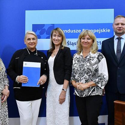 Członkowie Zarządu Województwa Śląskiego Rafał Adamczyk i Joanna Bojczuk wręczają listy gratulacyjne w ramach programu Fundusze Europejskie Śląskie 2021-2027. (wygenerowano przez AI)