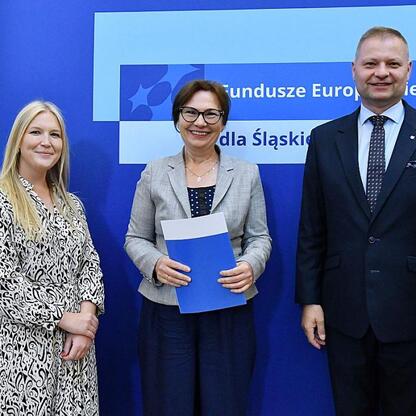 Członkowie Zarządu Województwa Śląskiego Rafał Adamczyk i Joanna Bojczuk wręczają listy gratulacyjne w ramach programu Fundusze Europejskie dla Śląskiego 2021-2027. (wygenerowano przez AI)