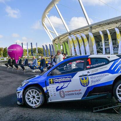 Rally car z hashtagiem #rajdslaska i logo European Rally Trophy, stojące przed Stadionem Śląskim w Katowicach. (wygenerowano przez AI)