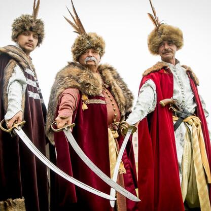 Trzech ludzi w strojach historycznych, uczestniczących w rekonstrukcji średniowiecznej, na tle namiotów i otwartego terenu. (wygenerowano przez AI)