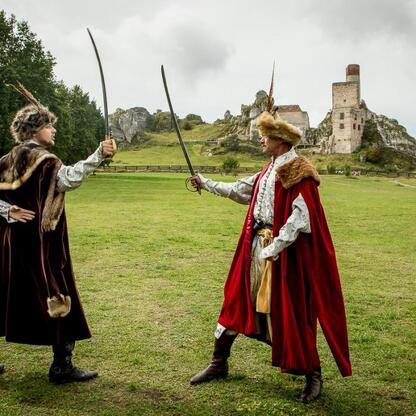 Dramatyczna scena z mieczami w polu, z tłem zamku i festiwalu Juromania. (wygenerowano przez AI)