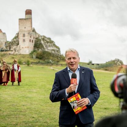 Marszałek Wojciech Saługa prowadzi konferencję prasową na błoniach zamku w Olsztynie, podkreślając bogactwo kulturowe i historyczne regionu. (wygenerowano przez AI)
