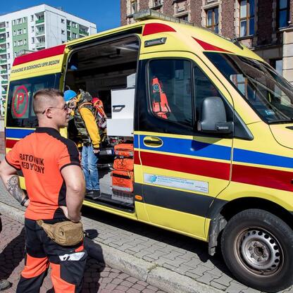 Paramedici w pomarańczowych mundurach ładują sprzęt medyczny z żółtego ambulansu na ulicy miasta. (wygenerowano przez AI)