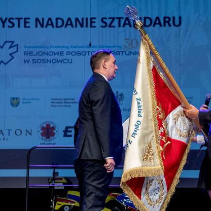 Marszałek Wojciech Saługa prezentuje sztandar SPZOZ Rejonowego Pogotowia Ratunkowego w Sosnowcu. (wygenerowano przez AI)