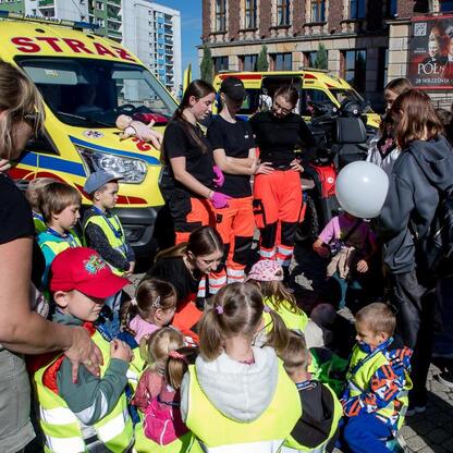 Z okazji jubileuszu 30-lecia SPZOZ Rejonowego Pogotowia Ratunkowego w Sosnowcu, dzieci i dorosli uczestniczą w edukacyjnej akcji przed ambulancem. (wygenerowano przez AI)