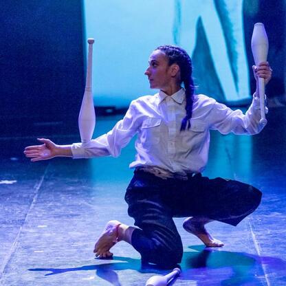 Performer na scenie z białymi klubami, wokół niego niebieskie światło, Kulturatrium residency, Śląsk. (wygenerowano przez AI)
